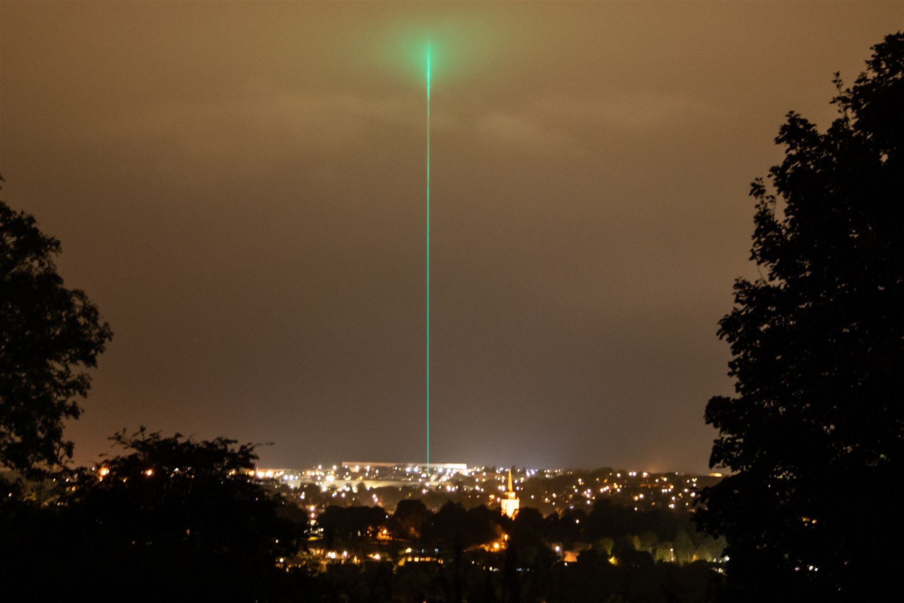 A green laser beam rises into the sky above a town at night