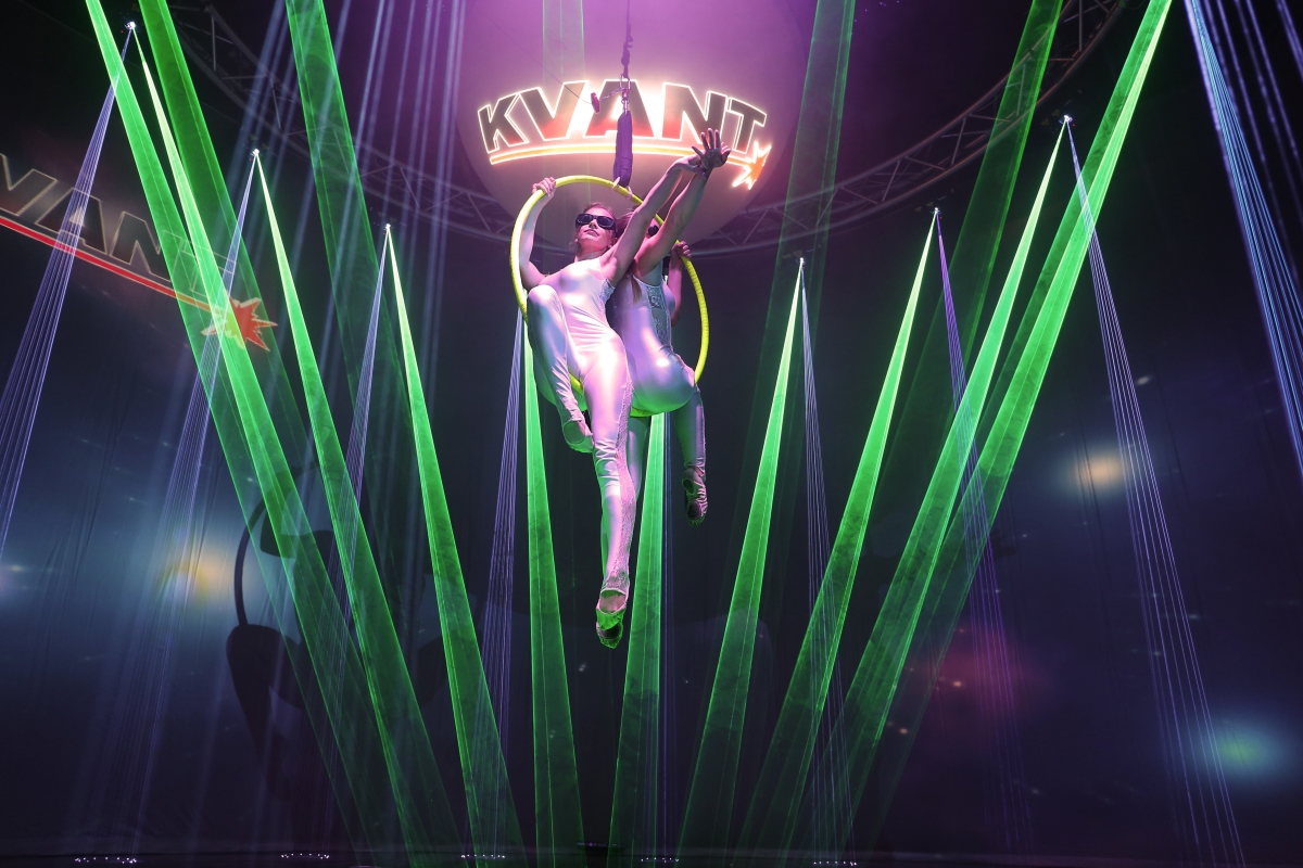 Green and violet laser beams around an indoor aerial performance
