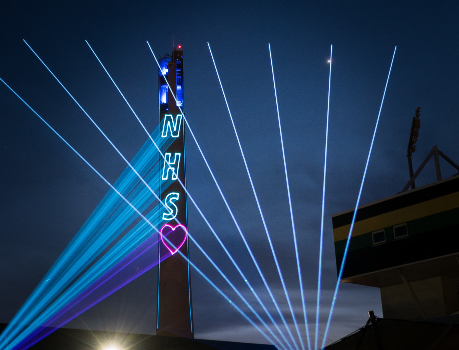 Blue laser beams around the Lift Tower with an NHS heart projection
